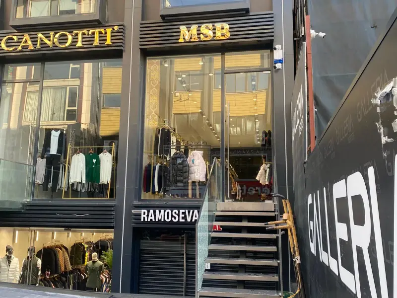 Siyah lamel cephe paneli üzerinde altın renk paslanmaz harfler, mağaza girişi