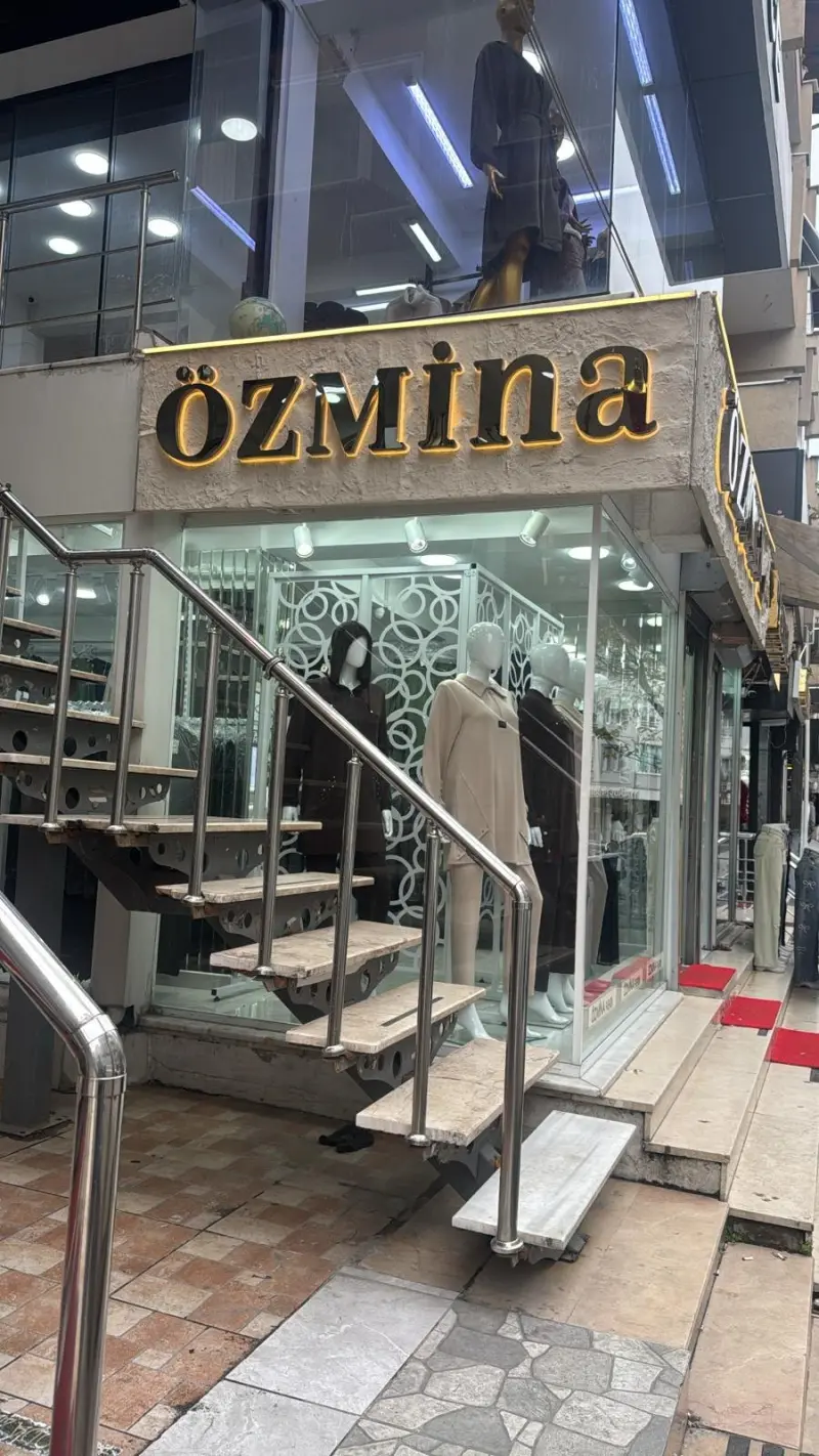 Taş sıva panel üzerinde siyah harfler ve arkasında sarı ışık halesi, köşe mağaza