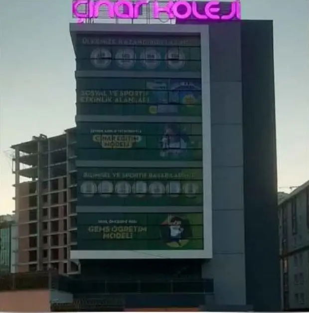 Okul binasının çatısında ışıklı pembe harfler ve baskılı panellerle giydirilmiş cephe, alacakaranlık