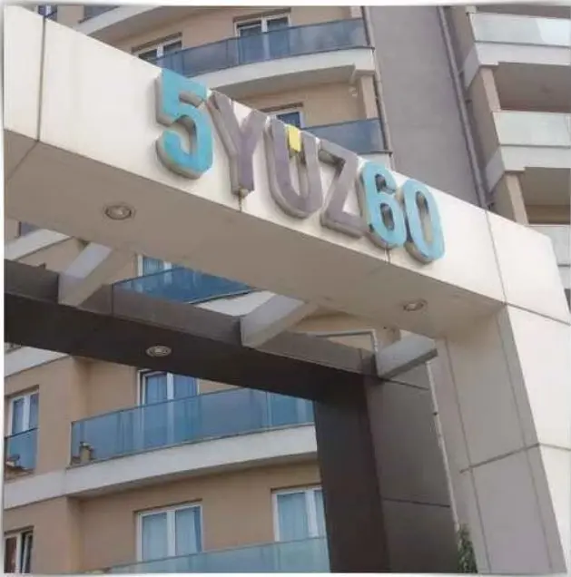 Konut sitesi girişinde beyaz saçak üzerinde renkli ışıksız kabartma harfler