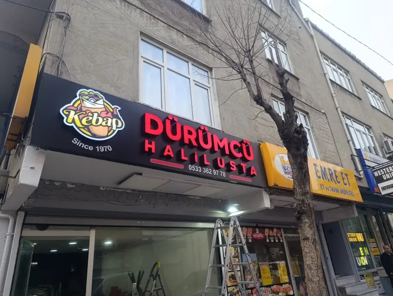 Siyah panel üzerinde kırmızı kutu harfler ve ışıklı renkli logo, restoran cephesi