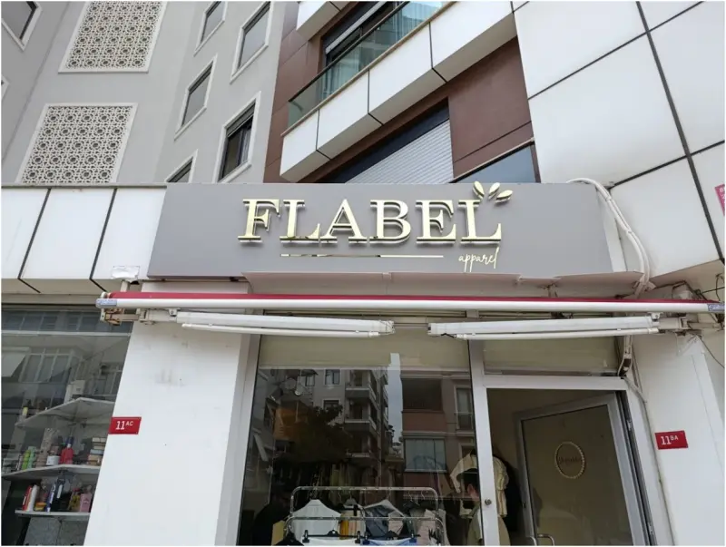 Gri panel üzerinde altın ayna paslanmaz harfler ve el yazısı alt satır